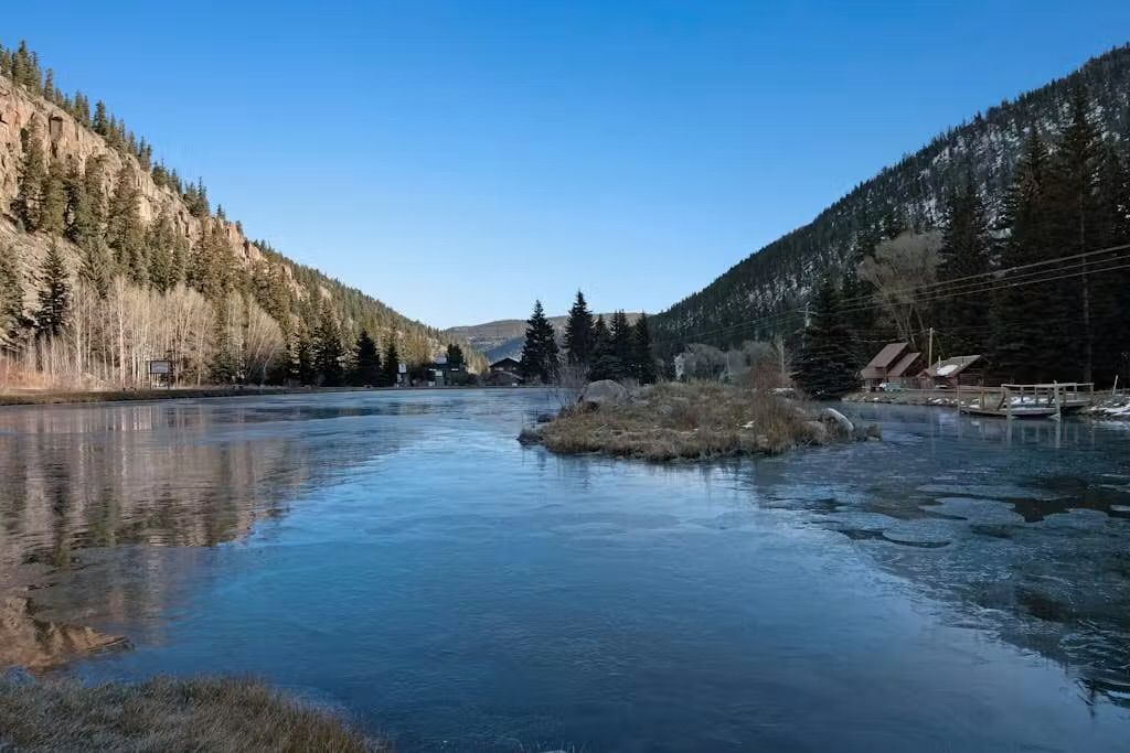 A river with a small island, surrounded by forested hills and a clear sky.