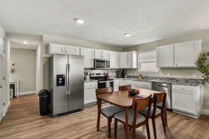 A modern kitchen with white cabinetry, stainless steel appliances, and a dining area with wooden chairs. - New & Modern 3BR/2BA | Family-Friendly Wilmington (Wilmington)