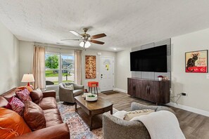 A living room with a brown leather couch, a grey armchair, a coffee table, and a ceiling fan. - New & Modern 3BR/2BA | Family-Friendly Wilmington (Wilmington)