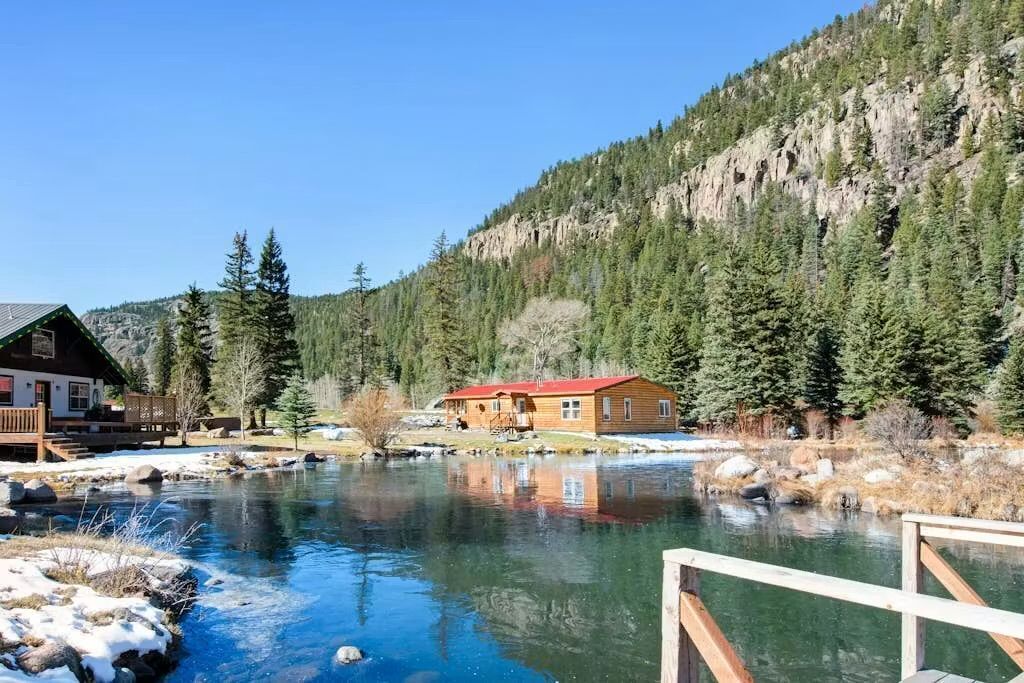Une cabane avec un toit rouge et une terrasse en bois donnant sur une rivière.