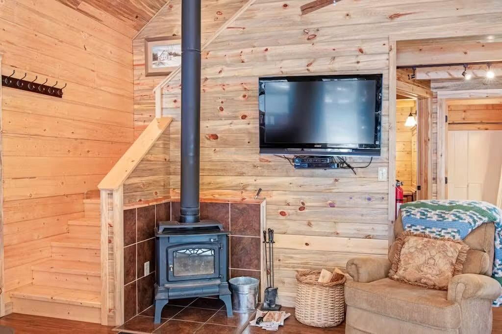 A cozy living room with a wooden interior, a fireplace, a television mounted on the wall, and a comfortable seating area.