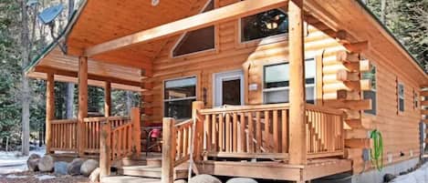 Une cabane en rondins avec un porche, une porte d’entrée et une cheminée.