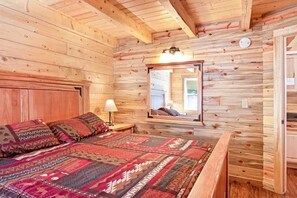 Une chambre rustique en bois, avec un lit, une table de chevet, une lampe et un miroir au mur.