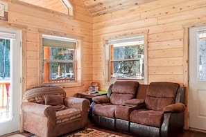 Ein Holzblockhaus-Innenraum mit einem Ledersessel, einem gemusterten Sessel und einem kleinen Tisch mit Büchern.