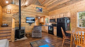 L’intérieur d’une cabane comprend une cheminée, une cuisine, un coin repas et un téléviseur.