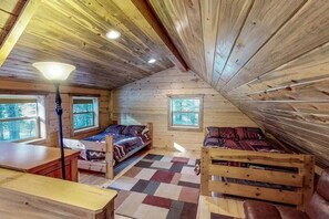 Eine Hütte mit geneigtem Dach, Holzwänden und einem Schachbrettfußboden, mit zwei Betten mit gemusterten Betttextilien.