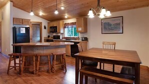 A kitchen with wooden cabinets, a refrigerator, a microwave, and a dining area with a wooden table and chairs. - Sequoia Cabin | Waterfront Escape with Private Hot (South Fork)