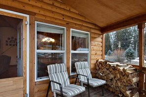 Une cabane en rondins avec deux chaises près des fenêtres, une cheminée et une pile de bois de chauffage.