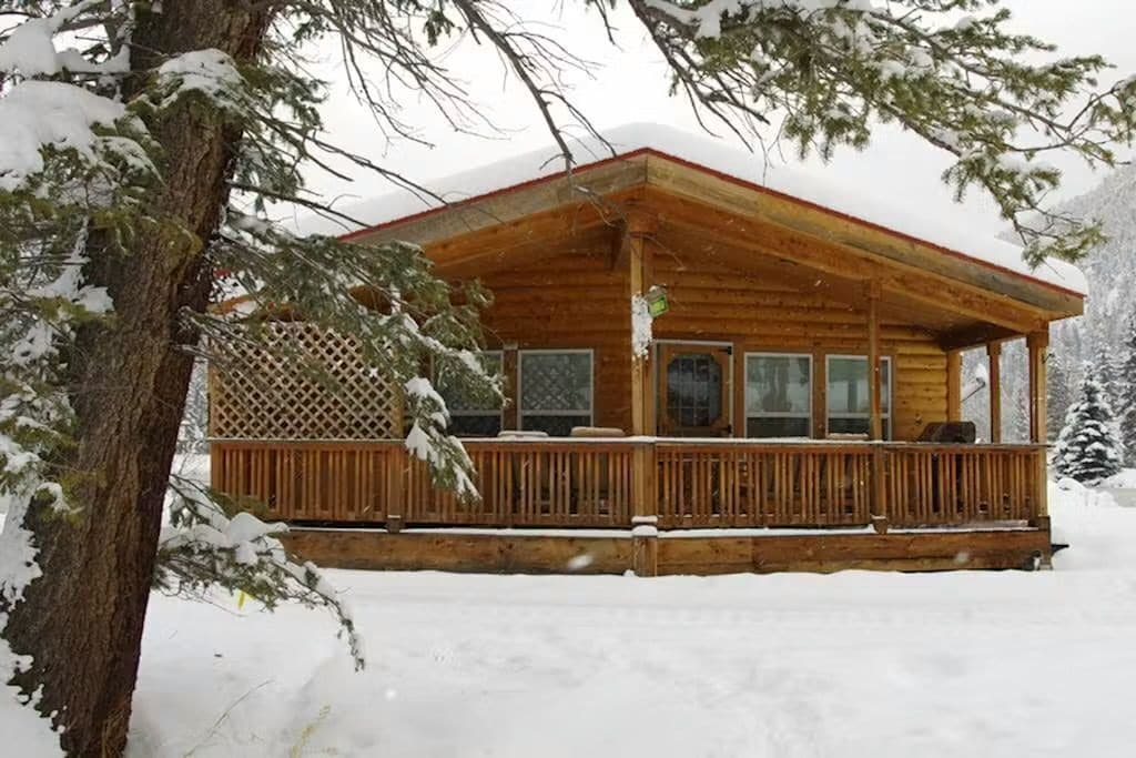 A wooden cabin with a porch, surrounded by snow-covered trees.