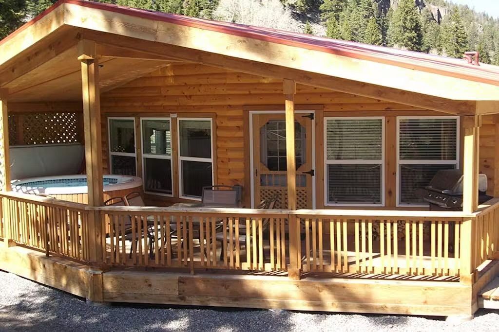 A wooden cabin with a covered porch, a hot tub, and a grill area.