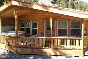 A wooden cabin with a covered porch, a hot tub, and a grill area. - Sequoia Cabin | Waterfront Escape with Private Hot (South Fork)