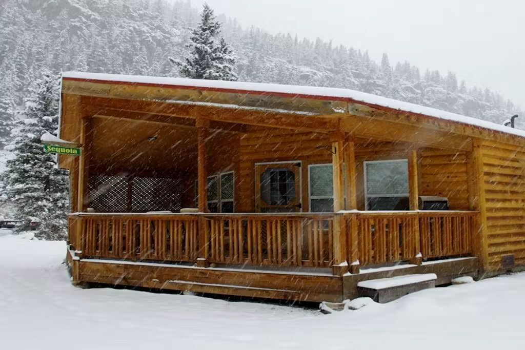 Eine Holzhütte mit Veranda, umgeben von schneebedeckten Bäumen.