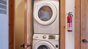 A compact laundry area with two stacked washing machines and a fire extinguisher mounted on the wall. - Sequoia Cabin | Waterfront Escape with Private Hot (South Fork)