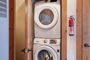 A compact laundry area with two stacked washing machines and a fire extinguisher mounted on the wall. - Sequoia Cabin | Waterfront Escape with Private Hot (South Fork)