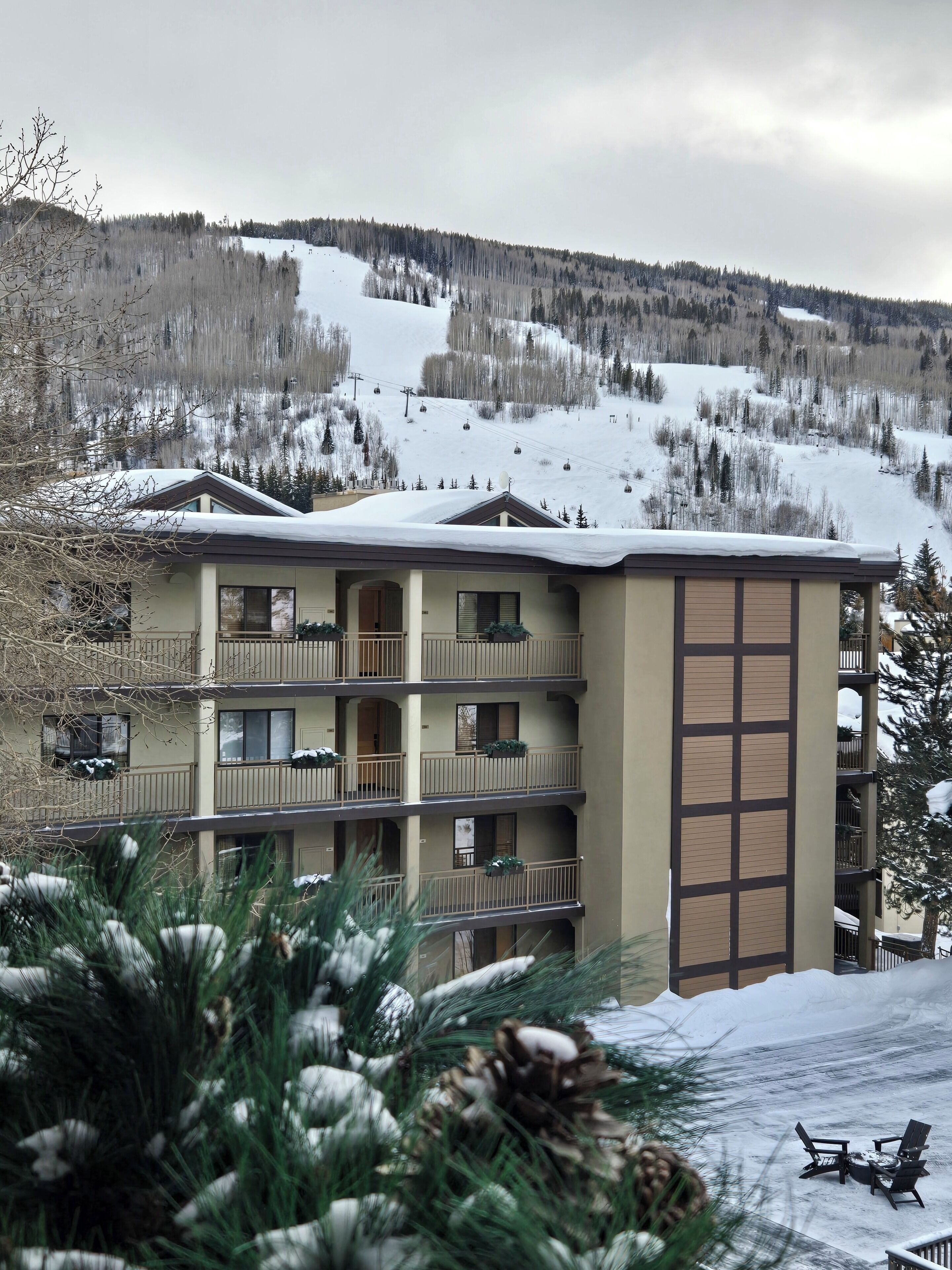 A multi-story hotel with balconies, a ski lift in the background, and a snowy landscape.