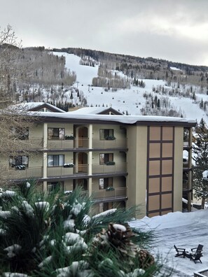 Un hotel de varios pisos con balcones, un telesilla de esquí al fondo y un paisaje nevado.