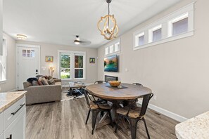 A spacious dining area with a wooden table and chairs, a ceiling fan, and a large window with a view of greenery. - Southeast Boise Deluxe Home (Boise)