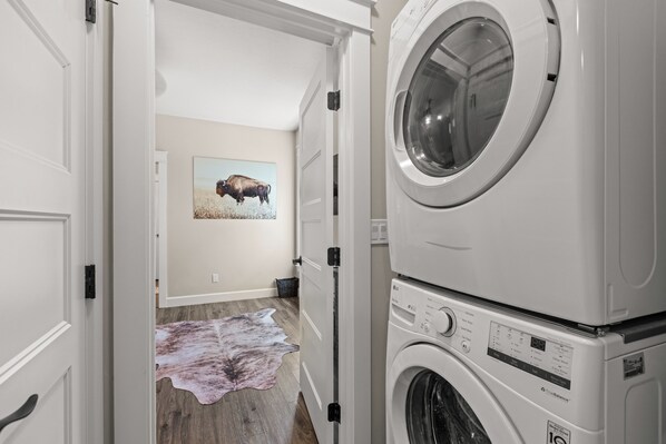 A laundry room with stacked washers and dryers, a buffalo painting on the wall, and a cowhide rug on the floor.