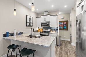 A modern kitchen with granite countertops, stainless steel appliances, and a central island with bar stools. - Southeast Boise Deluxe Home (Boise)