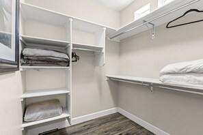 A walk-in closet with open shelving, a hanging rod, and a bed with a white comforter.