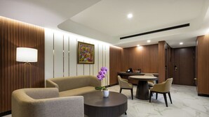 A modern hotel lobby with a sofa, round table, chairs, a potted orchid, and a painting on the wall. - The Royal Alana Yogyakarta Hotel & Convention Center (Ngaglik)