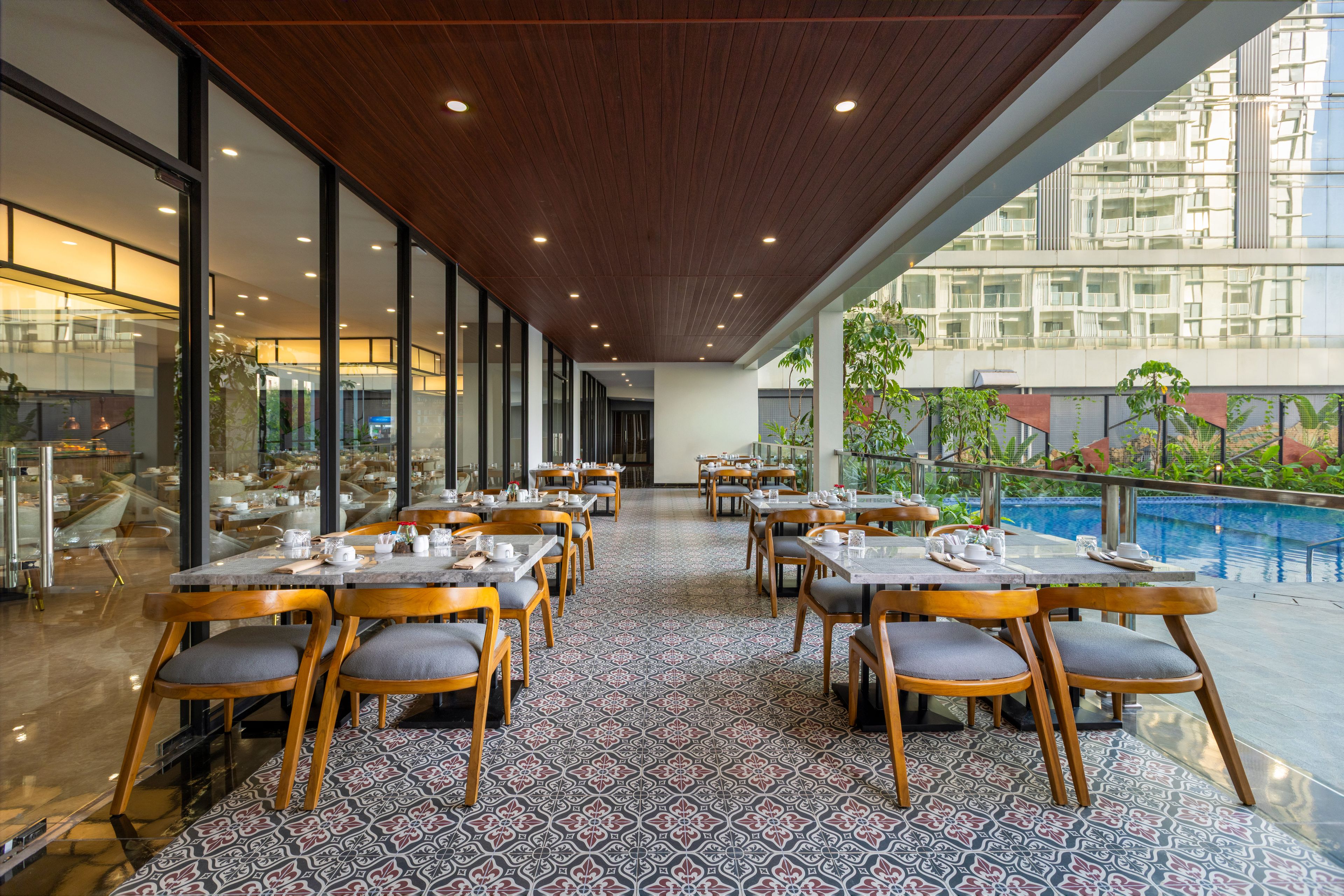 Un restaurante con vista a la piscina, que cuenta con un amplio salón comedor con mesas y sillas, piso estampado y techo de madera.
