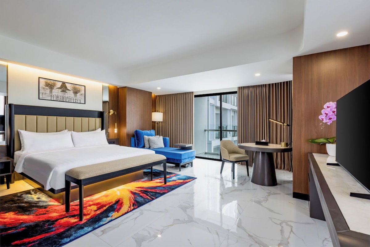 Quarto de hotel moderno com cama grande, escrivaninha, cadeira e vista para o exterior.