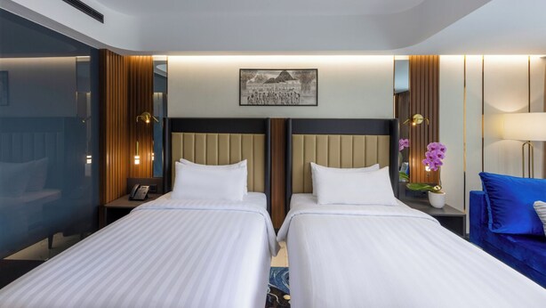 A hotel room with two beds, a large window, a painting on the wall, and a nightstand with a lamp. - The Royal Alana Yogyakarta Hotel & Convention Center (Ngaglik)