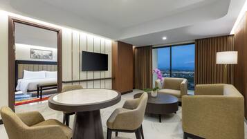 A hotel room with a bed, a TV, a dining table, and a view of the city.