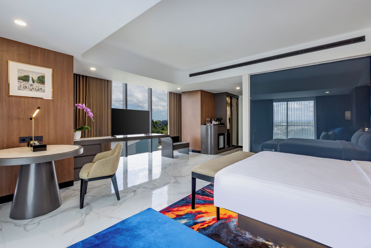 A modern hotel room with a bed, a desk, a chair, a television, and a view of the city.