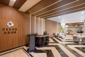 En hotellobby med en väggpanel av trä, en receptionsdisk och en matplats med bord och stolar.