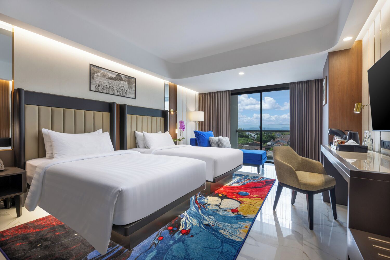 Habitación de hotel con dos camas, un escritorio, una silla, un televisor y un ventanal con vistas a la ciudad.