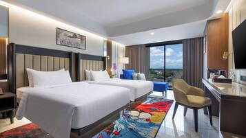 Habitación de hotel con dos camas, un escritorio, una silla, un televisor y un ventanal con vistas a la ciudad.