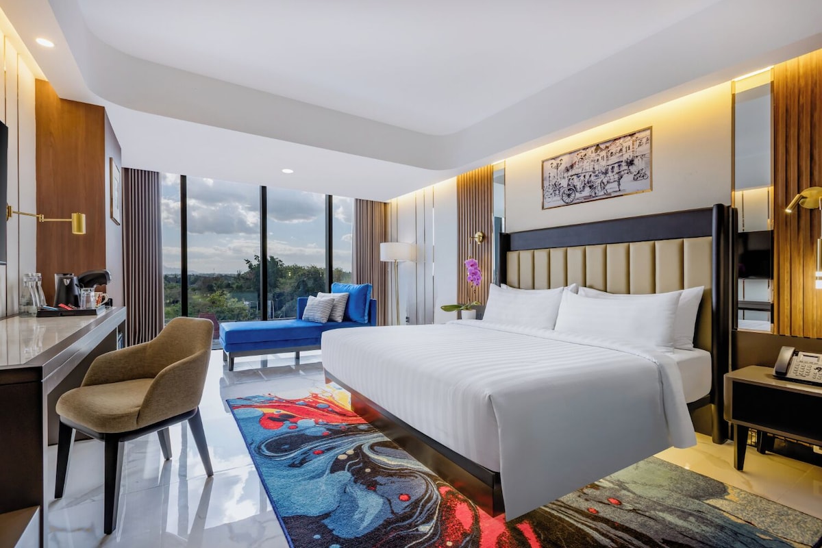 Quarto de hotel moderno com uma cama grande, uma escrivaninha, uma cadeira e vista para o exterior.
