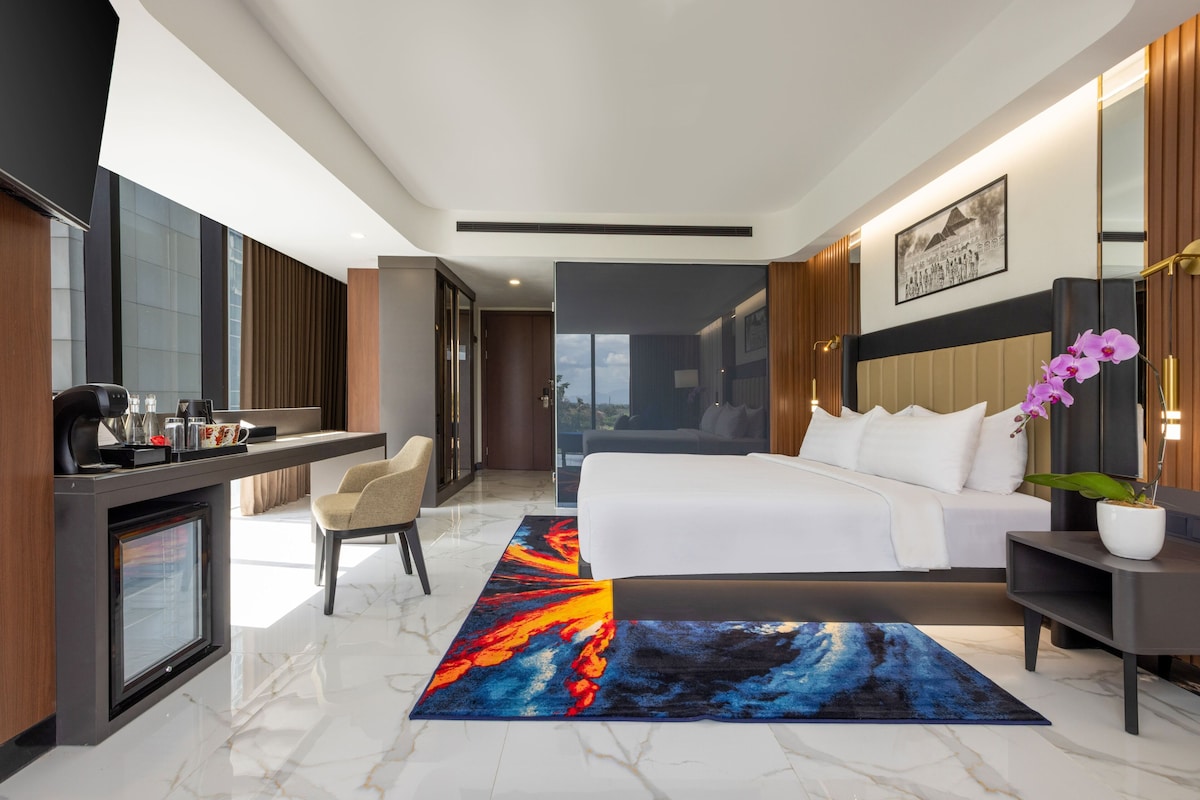 Quarto de hotel moderno com cama, mesa de cabeceira, escrivaninha, cadeira e vista para o exterior.