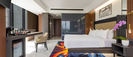 A modern hotel room with a bed, bedside table, desk, chair, and a view of the outdoors.