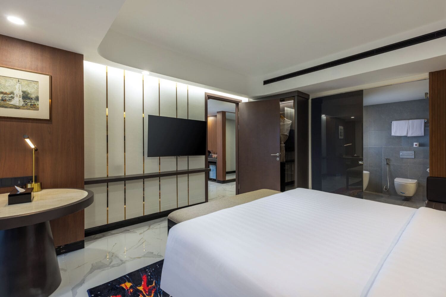 A modern hotel room with a large bed, a flat-screen TV, a bedside table, and a bathroom with a shower and toilet.