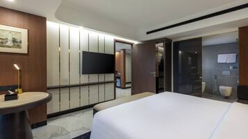 A modern hotel room with a large bed, a flat-screen TV, a bedside table, and a bathroom with a shower and toilet.