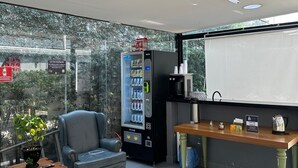 Habitación moderna con zona de estar, máquina expendedora, estación de café y vistas a través de amplios ventanales.
