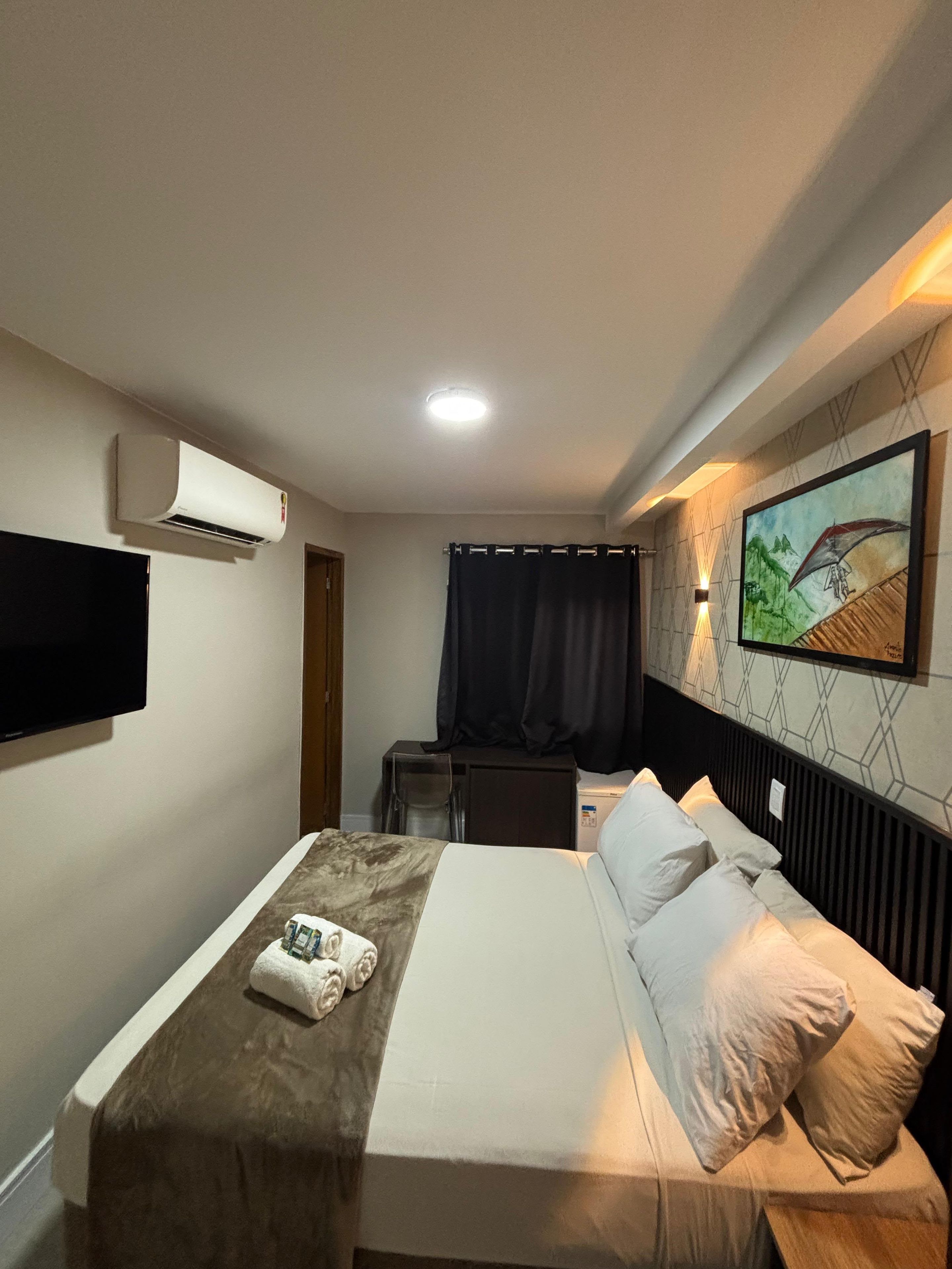 Habitación de hotel con cama, televisión de pantalla plana en la pared, aire acondicionado, escritorio con silla y un cuadro en la pared.