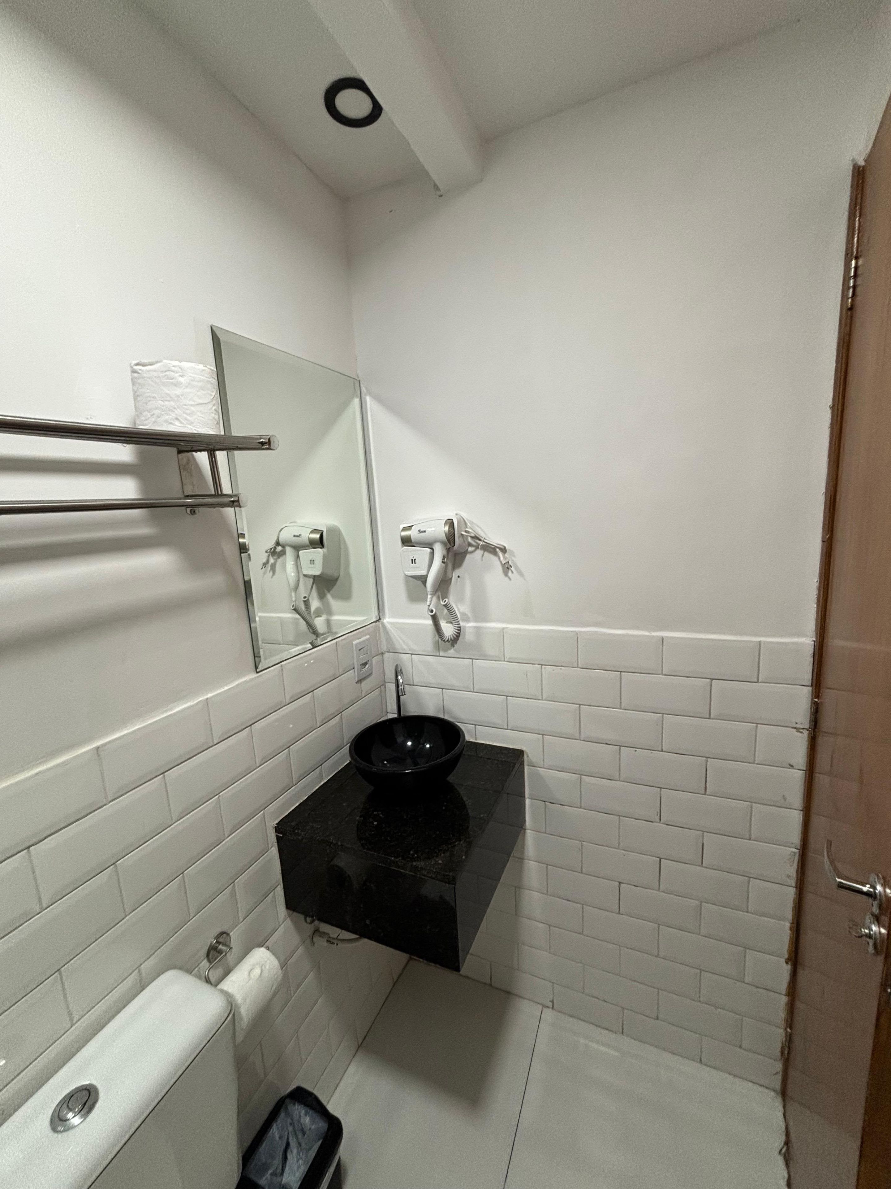 A bathroom with a black sink, white tiled walls, a mirror, and a towel rack.
