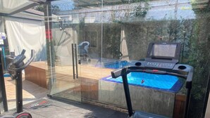 A home gym with a treadmill, stationary bike, and a small pool area.