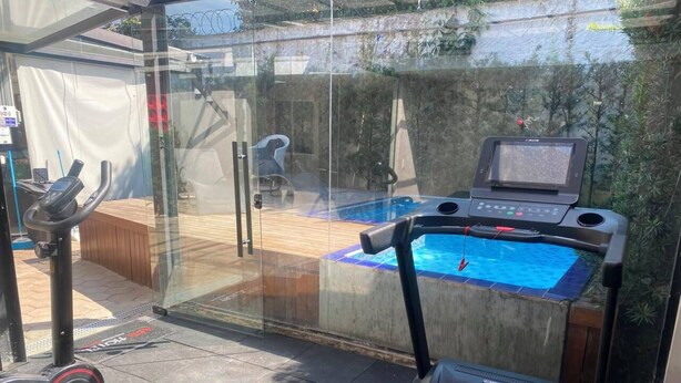 Un gimnasio en casa con cinta de correr, bicicleta estática y una pequeña zona de piscina.