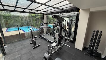 Academia com equipamentos de ginástica, um banco e uma barra de halteres.