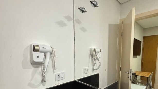 Casa de banho moderna com lavatório preto, espelho e dois secadores de cabelo fixados na parede.