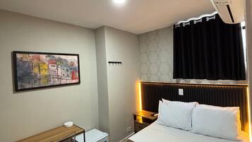 Habitación de hotel con cama, escritorio, silla, aire acondicionado de pared y un cuadro.