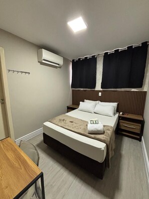 A bedroom with a bed, bedside tables, an air conditioning unit, a window with curtains, and a small table. - ADD HOTÉIS MORUMBI (São Paulo)