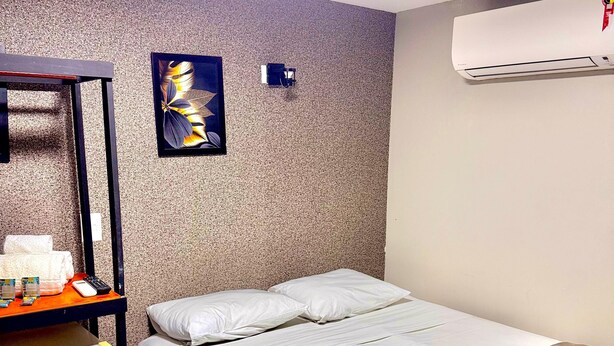 A hotel room with a bed, a desk with a computer, and a wall-mounted air conditioner.