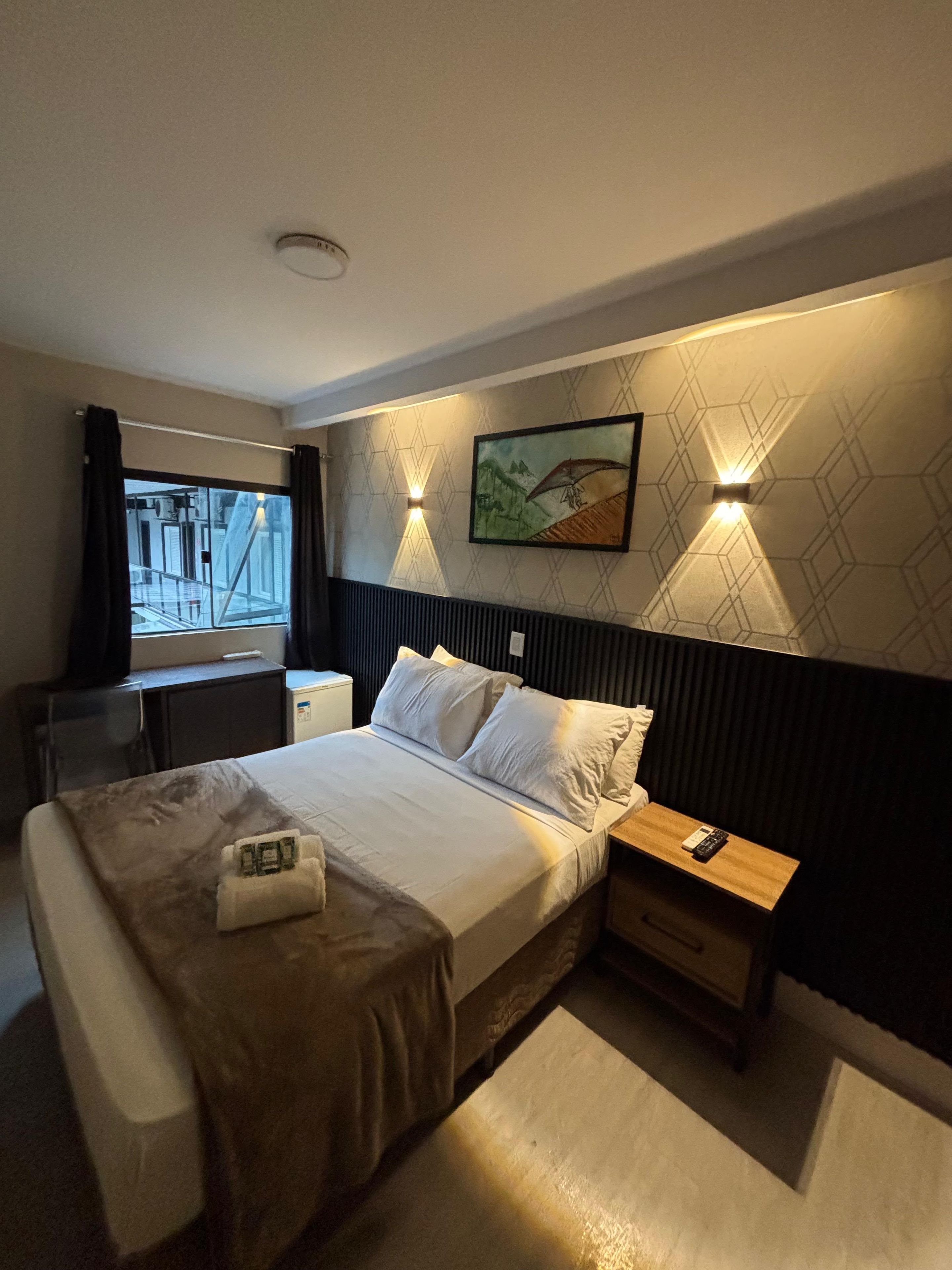 Una habitación de hotel con una cama, mesitas de noche, un escritorio y una ventana.