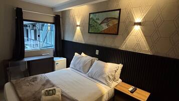 Una habitación de hotel con una cama, mesitas de noche, un escritorio y una ventana.